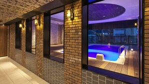 Un área de piscina interior moderna con paredes de ladrillo y grandes ventanales con vistas a una piscina exterior.