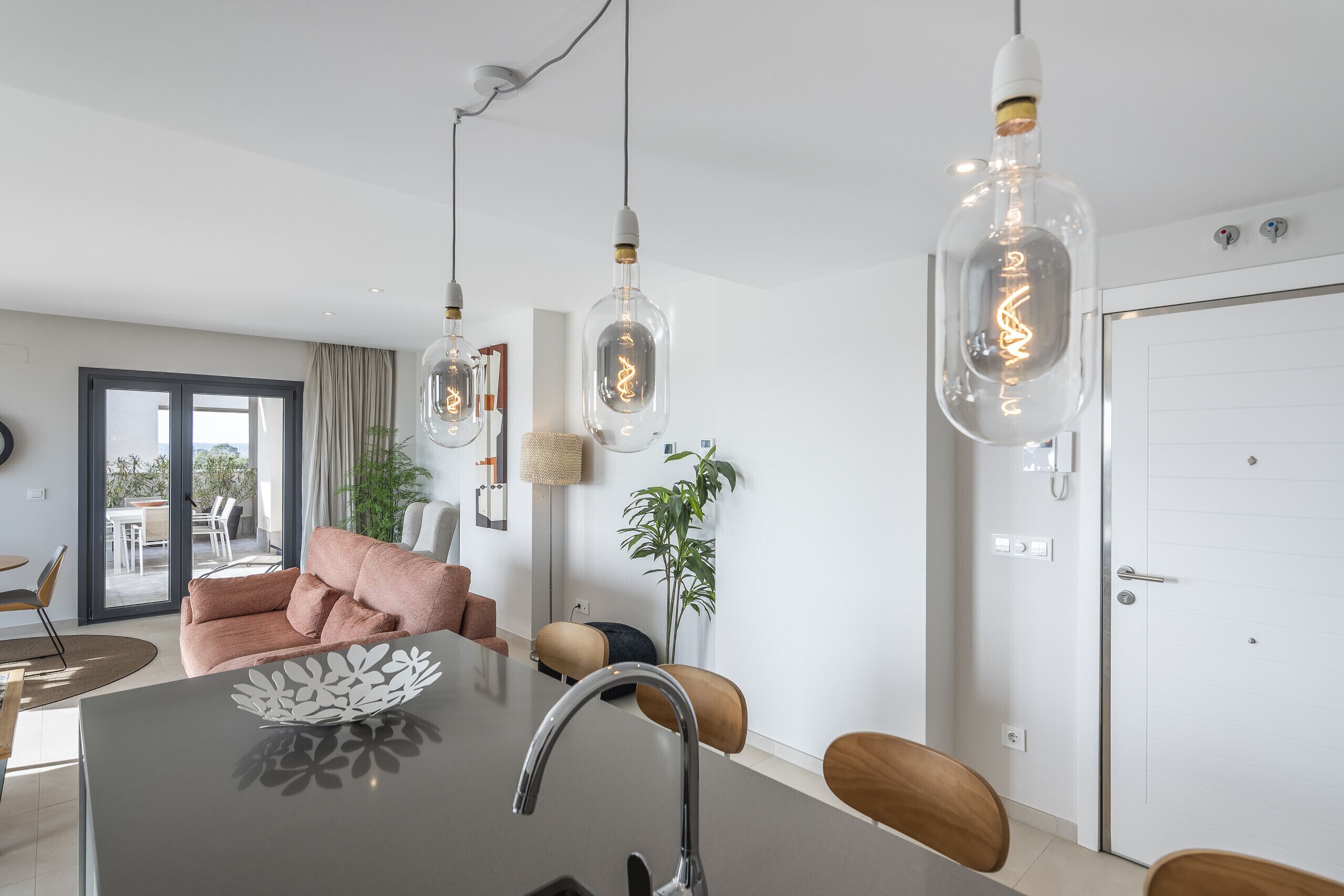 Una cocina moderna con una isla central, luces colgantes y un comedor con sillas.