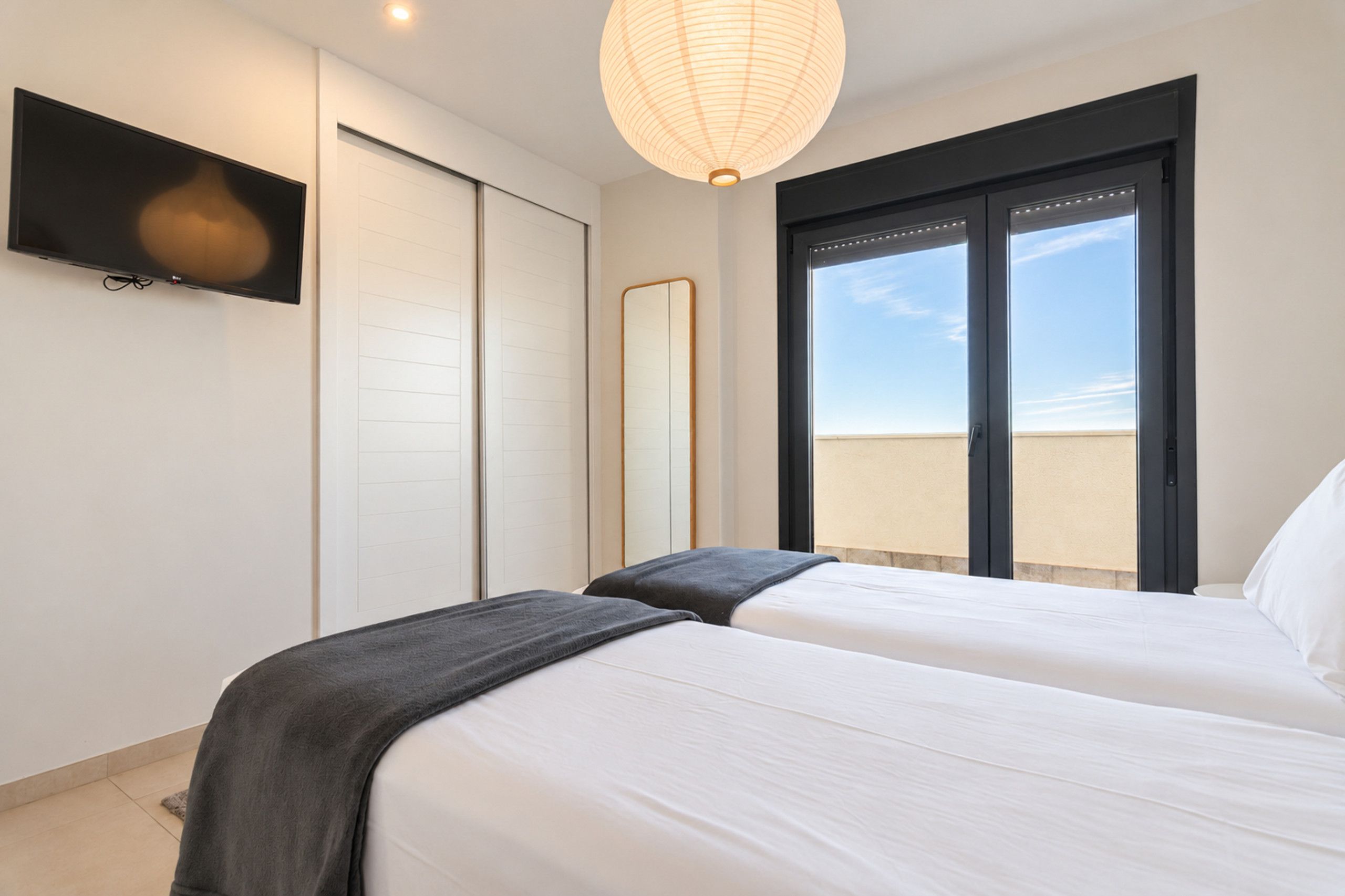 A hotel room with two beds, a TV, a large window, and a ceiling light.