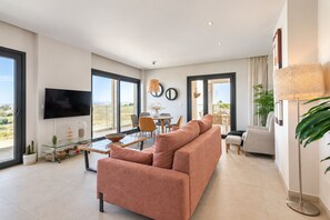 A modern living room with a large sofa, a flat-screen TV, and a dining area with chairs and a table.