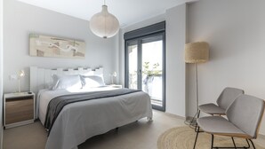 Une chambre à coucher moderne, avec un lit, des tables de chevet, une lampe sur pied et une vue dégagée sur l’extérieur grâce à une grande fenêtre.