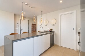 A modern kitchen with a central island, pendant lighting, and a dishwasher.