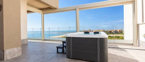 A modern outdoor hot tub area with a clear view of the sea and a cityscape in the background.