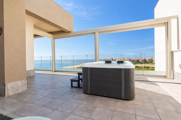 A modern outdoor hot tub area with a clear view of the sea and a cityscape in the background.