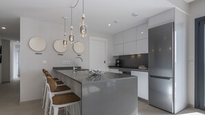 Une cuisine moderne dotée d’un îlot central, d’appareils électroménagers en acier inoxydable et de luminaires suspendus.