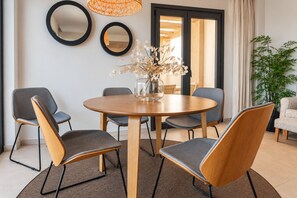 A modern dining area with a round wooden table, grey upholstered chairs, and a vase with dried flowers.