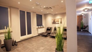 A modern spa room with a massage table, two large potted plants, a radiator, and a wall-mounted artwork. - DORMERO Hotel Bremen (Bremen)