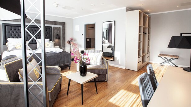 A modern hotel room with a bed, a sofa, a table, and a mirror. - DORMERO Hotel Bremen (Bremen)