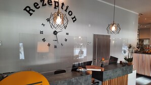 A reception area with a modern design, featuring a clock, a reception desk, and a wall with the word "Reception" above it. - DORMERO Hotel Bremen (Bremen)
