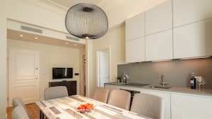 A modern kitchen with a dining area, featuring a marble table, grey upholstered chairs, a black pendant light, and a built-in TV. - Florence Luxury Apartment al Duomo by Mmega (Florence)