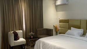 Ein modernes Hotelzimmer mit einem großen Bett, einer Sitzecke mit einem Sessel, einem kleinen Tisch und einer Topfpflanze.