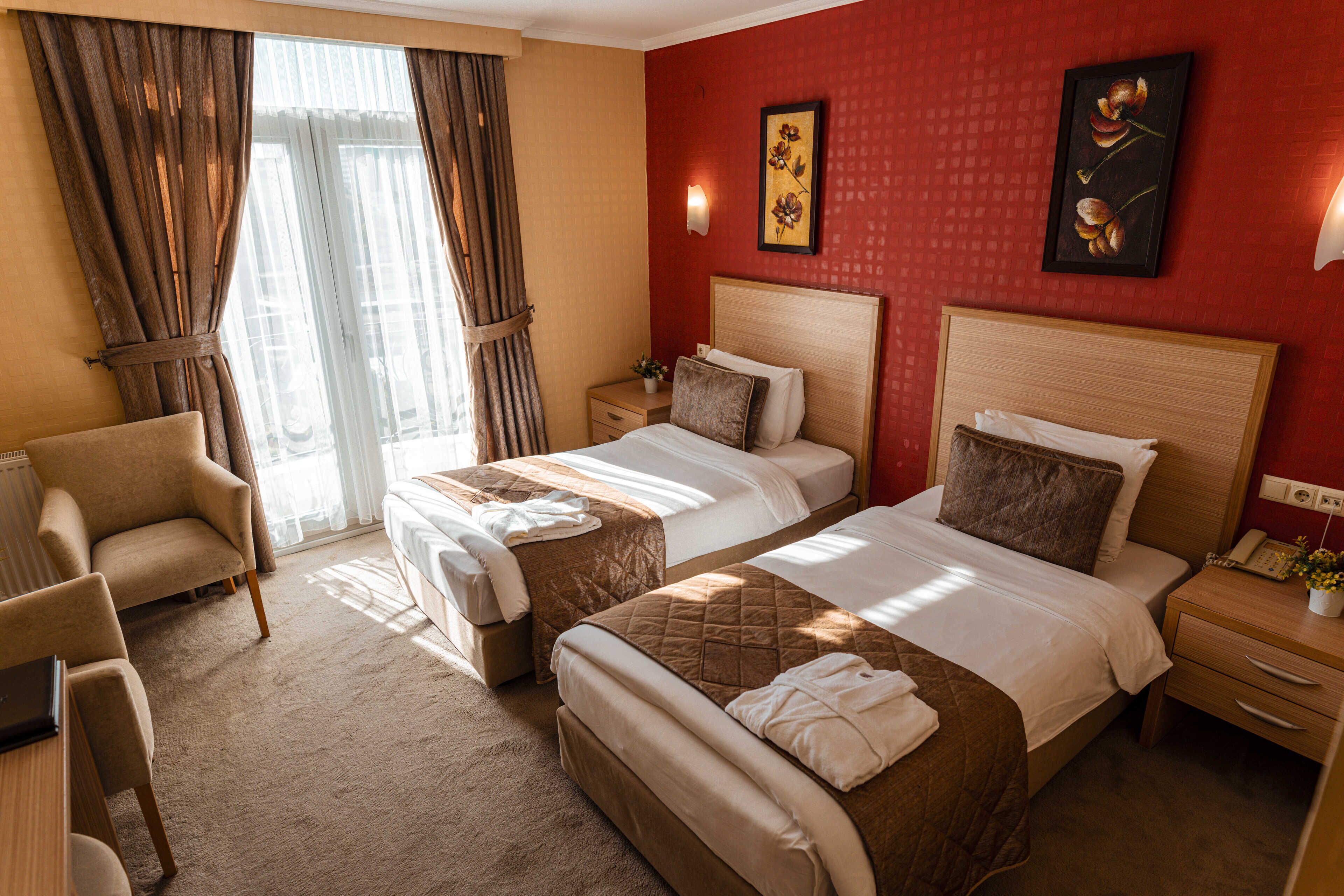 A hotel room with two beds, a desk, a chair, and a window with curtains.