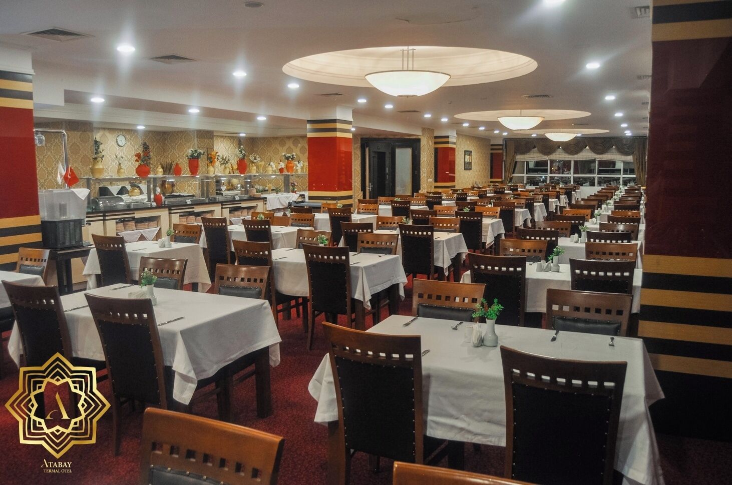 Un restaurant spacieux, doté de nombreuses tables et chaises, d’une horloge au mur et d’un mur décoratif orné de fleurs.