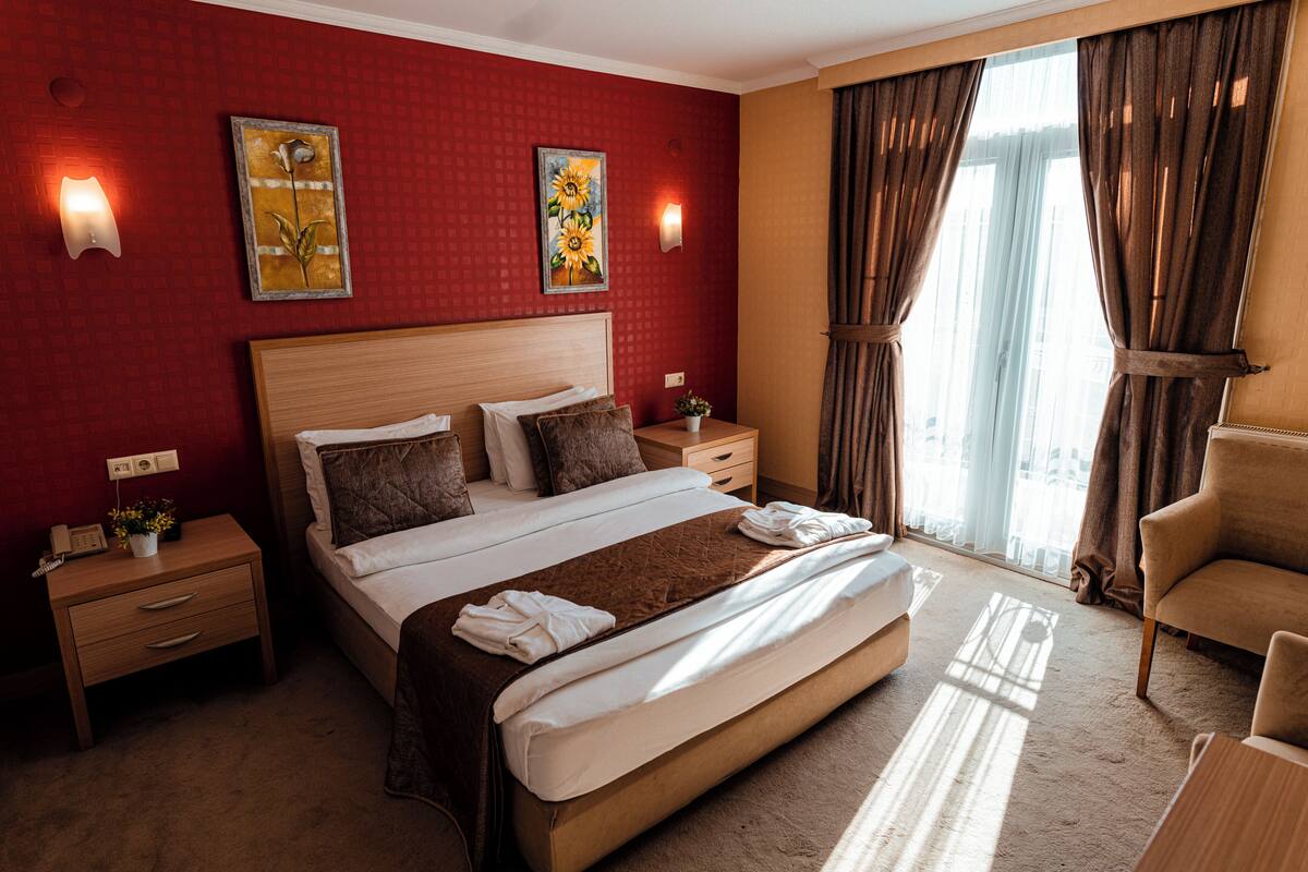 A hotel room with a large bed, two bedside tables, a nightstand, a chair, and a window with curtains.
