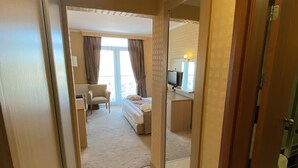 A hotel room with a bed, a desk, a chair, a TV, and a large mirror. - Atabay Termal Hotel (Kozakli)