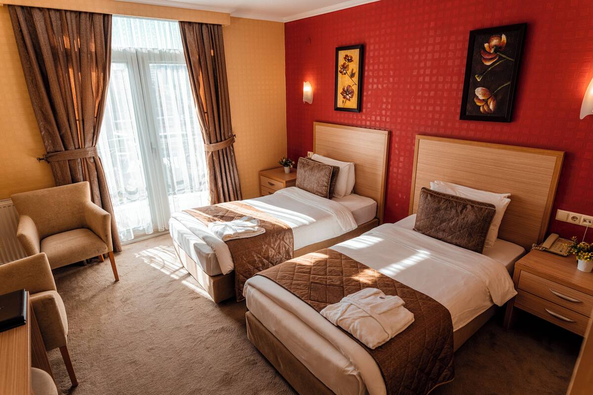 A hotel room with two beds, a desk, a chair, a nightstand, and a window with curtains.