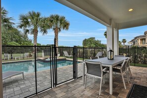 Relax by the pool surrounded by lush greenery and palm trees, with a glass fence offering a clear view.