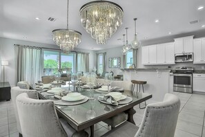 Formal dining area with a large table for six, surrounded by upholstered chairs and crystal chandeliers.