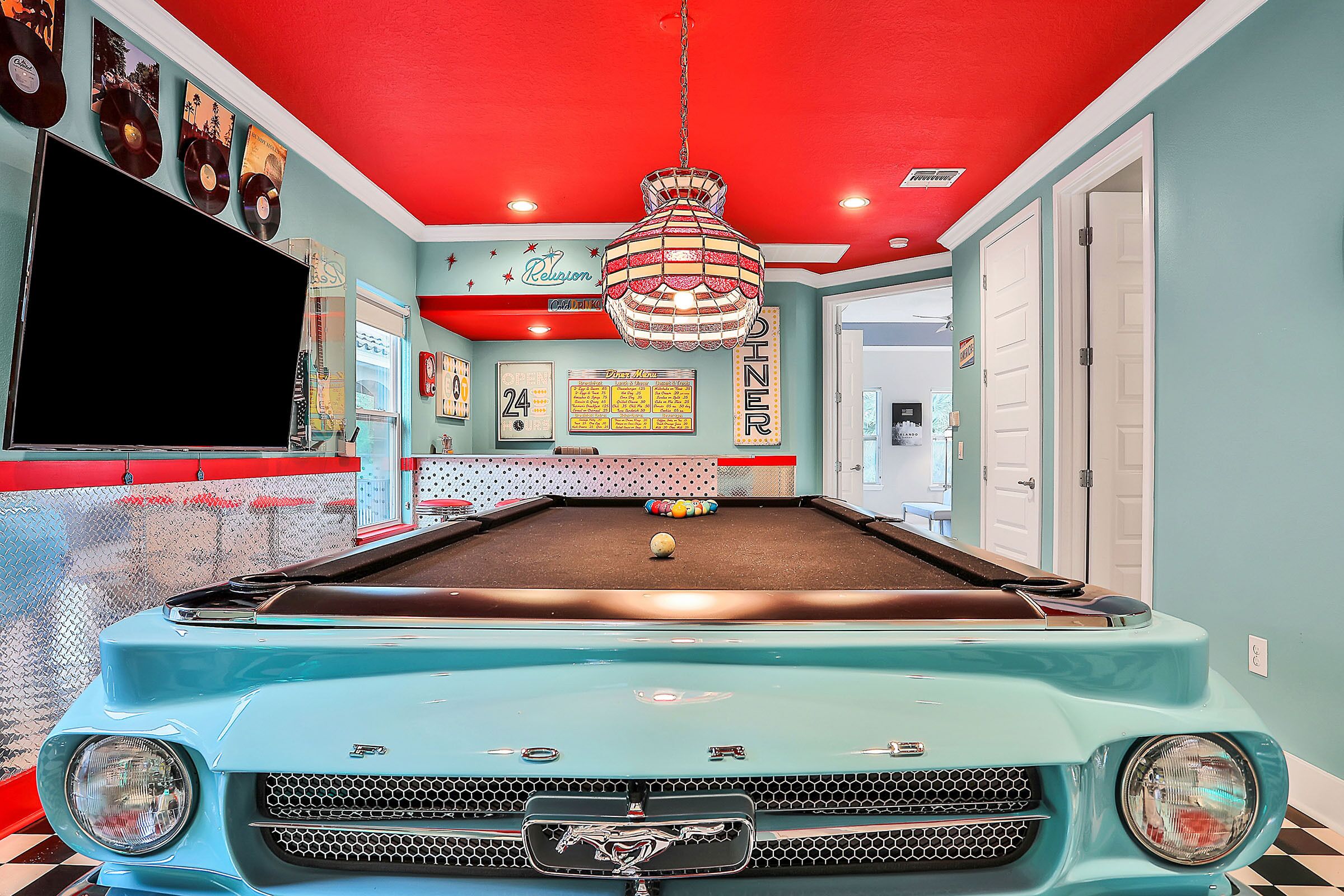A pool table with a vintage car design, a television, and a billiards cue rack.