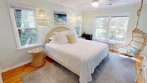 A bedroom with a large bed, two windows, a ceiling fan, and a hanging chair. - Classic Beach Cottage~Surf Shack (Folly Beach)