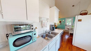 A kitchen with white cabinets, a turquoise microwave, a toaster, a sink, and a refrigerator. - Classic Beach Cottage~Surf Shack (Folly Beach)