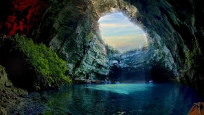 Eine Höhle mit einem natürlichen Bogen, der zu einem Gewässer führt, umgeben von Grünpflanzen.