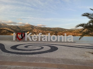 Ein Schild mit dem Wort 'Kefalonia' und einem Herzsymbol, umgeben von einem dekorativen Bereich mit spiralförmigem Muster.