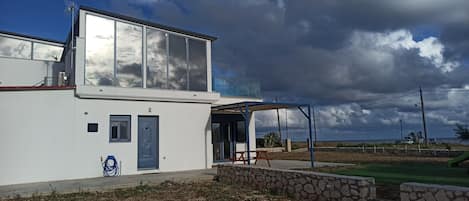 A modern two-story house with a balcony, a stone wall, and a clear view of the sky.