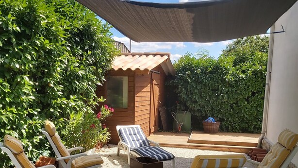 A patio area with outdoor seating, a wooden shed, and a shaded area.