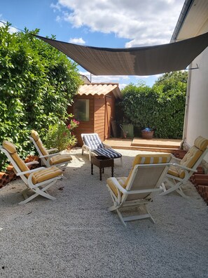 Un patio con mobiliario exterior, un cobertizo de madera y una zona con sombra.