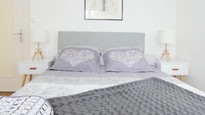 A bedroom with a bed, two bedside tables with lamps, a framed picture on the wall, and a door.