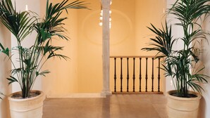 A hallway with two large potted plants, a tiled floor, and a railing with a balustrade.