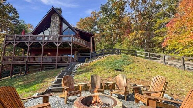 Eine Lodge mit Kamin aus Stein, umgeben von Holzstühlen, einem Steineinsatz für ein offenes Feuer und einer Holzterrasse mit einer Treppe zu einem überdachten Bereich.