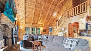Ein gemütliches Blockhaus-Interieur mit einem großen grauen Sofa, einem kleinen Holztisch und einem Kamin aus Stein.