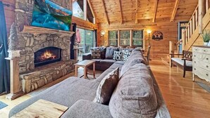 Ein gemütliches Blockhaus-Interieur mit Kamin aus Stein, Holzboden und einem großen Fernseher darüber.