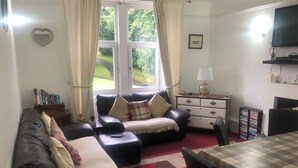 A living room with a sofa, a coffee table, a TV, and a bookshelf. - Captivating 2-bed Apartment in Isle of Bute (Rothesay)
