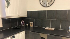 A compact kitchen with a washing machine, a clock, and a bar stool. - Captivating 2-bed Apartment in Isle of Bute (Rothesay)