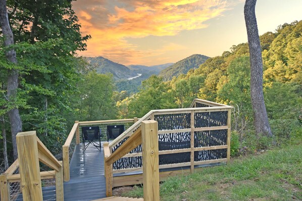 Una terraza de madera con barandilla que conduce a un área de estar cubierta y vistas a un valle.