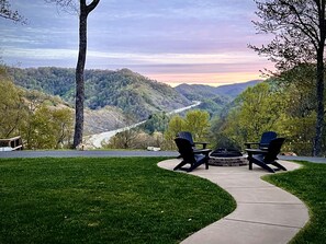 Une terrasse avec deux fauteuils Adirondack et un foyer extérieur, donnant sur une vallée où serpente une route et s’étendent des collines.