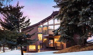 Un edificio moderno de varios pisos con amplios ventanales y balcones, rodeado de nieve y árboles.