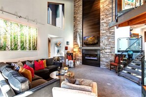 Amplia sala de estar con chimenea, un cuadro grande y una escalera que sube a un nivel superior.