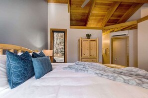Un dormitorio con cama, cabecera de madera, armario, puerta y ventana con vistas a árboles.