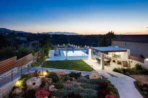A landscaped outdoor area with a swimming pool, stone building, and a wooden deck. - Five Bedroom Villa with Private Pool (Rethymno)