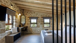 Ein Schlafzimmer mit Steinwänden, Holzbalkendecke, einem Bett mit aufgerollten Handtüchern, einem Schreibtisch mit Stuhl und einem großen Spiegel.