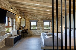 A bedroom with stone walls, a wooden ceiling, a bed with rolled towels, a desk with a chair, and a large mirror. - Five Bedroom Villa with Private Pool (Rethymno)
