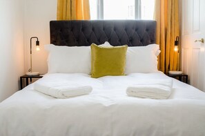 A neatly made bed with white linens and two pillows, one green and one white, in a room with a tufted headboard and two bedside lamps. - π Bright & Spacious Margate Home β Just Minutes from the Beach ποΈ (Kent)