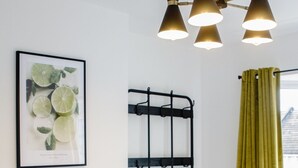 Et hotelværelse med en seng, en sort metalreol, et indrammet billede af limefrugter og en grøn gardin.