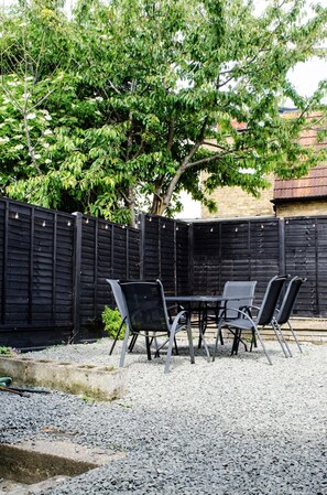 An outdoor seating area with a table and chairs, surrounded by a gravel ground and a wooden fence.