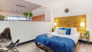 A modern hotel room with a large bed, two bedside lamps, a wooden headboard, and a view of the city through large windows. - Stay Angels Blonk Street Apartments (Sheffield)