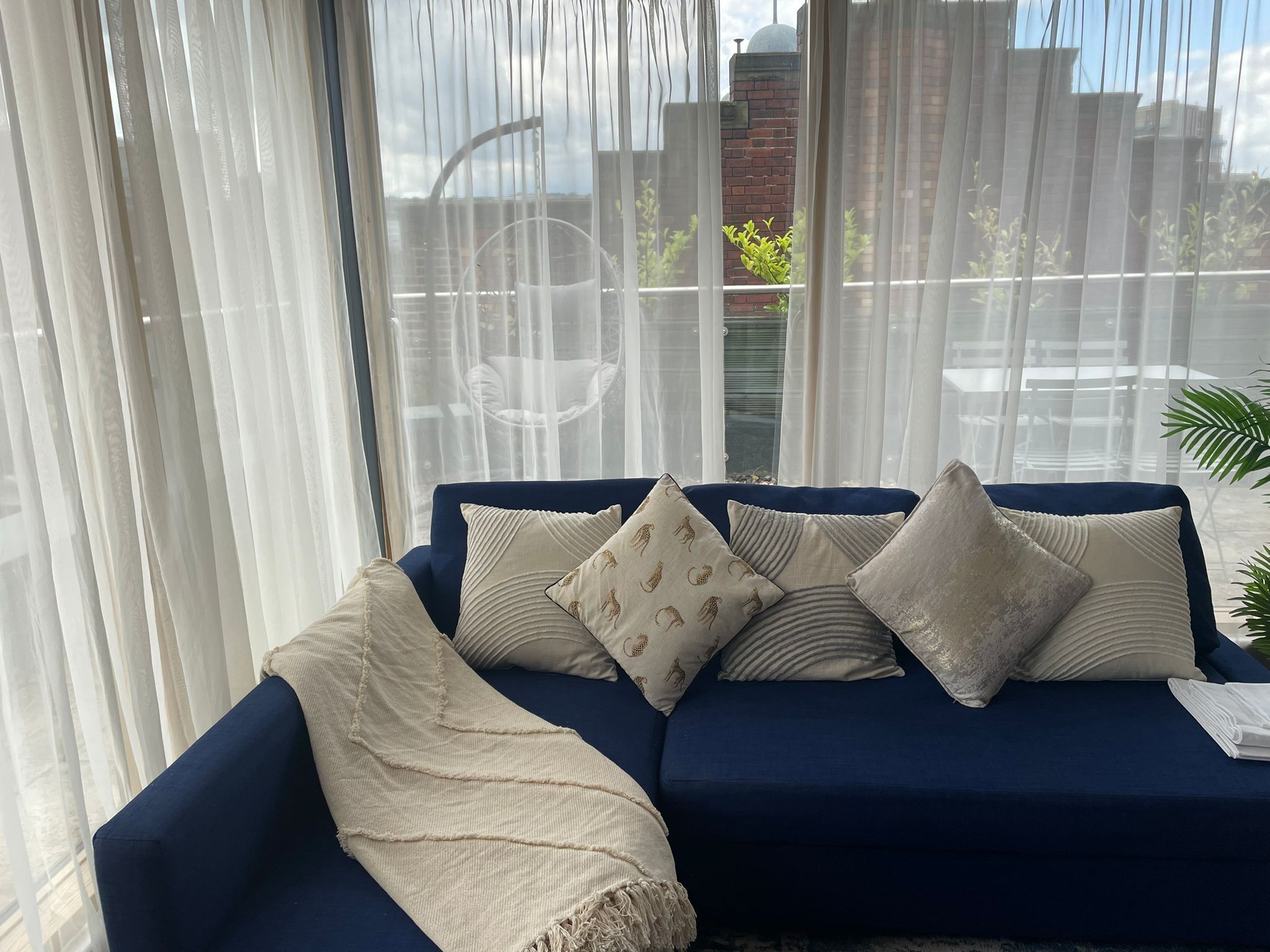 A blue sofa with patterned cushions and a sheer white curtain.